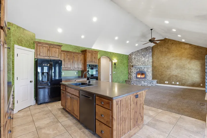 Open-concept kitchen and living area featuring a stone fireplace, vaulted ceilings with recessed lighting and a ceiling fan, and a kitchen island with integrated sink and dishwasher