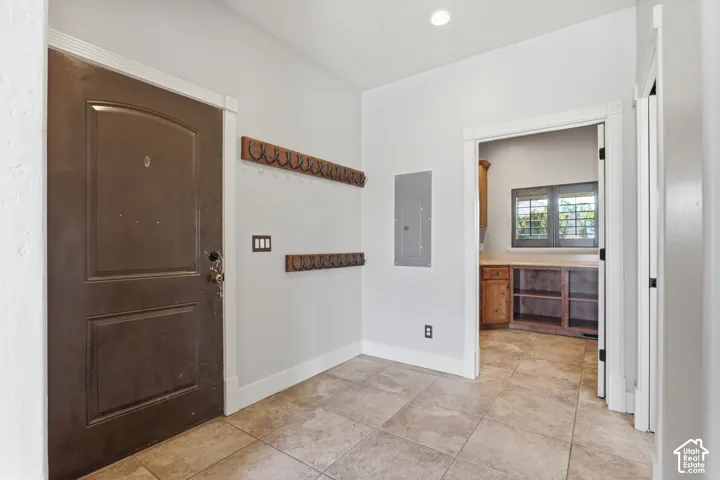 Entryway featuring natural tile flooring, a solid panel door with arched detailing, and two wall-mounted coat racks