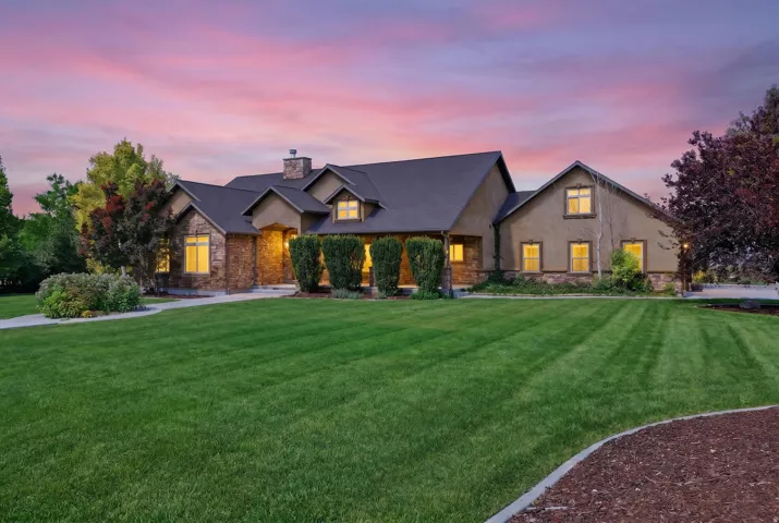 Stucco and stone facade home featuring a dark shingle roof, a prominent chimney, and multiple gables