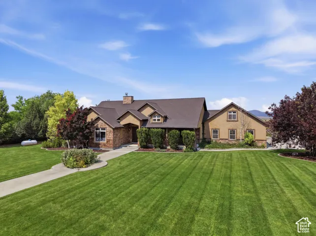 Spacious front yard with a stone and stucco exterior, dark shingle roof, mature landscaping, and an extended concrete driveway