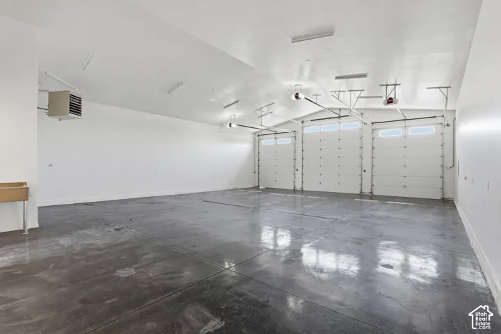 Spacious garage featuring three overhead doors with window panels, polished concrete flooring, overhead fluorescent lighting, and a wall-mounted utility sink