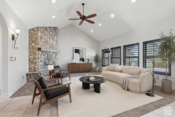 Vaulted ceiling living area featuring a prominent stone fireplace, multiple windows with dark shutters, recessed lighting, and a dark wood ceiling fan
