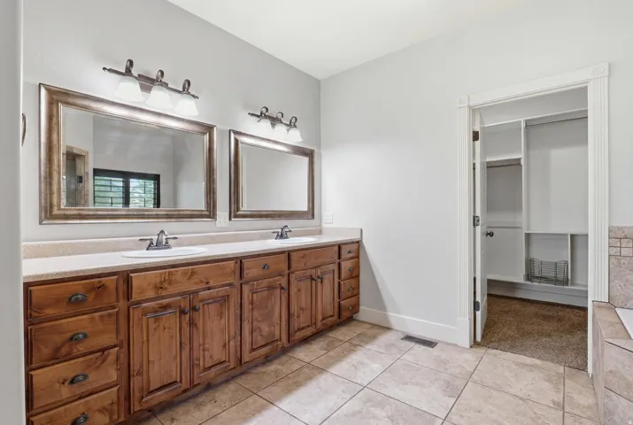 Double vanity featuring wood cabinetry, integrated sinks, and individual mirrors with overhead lighting