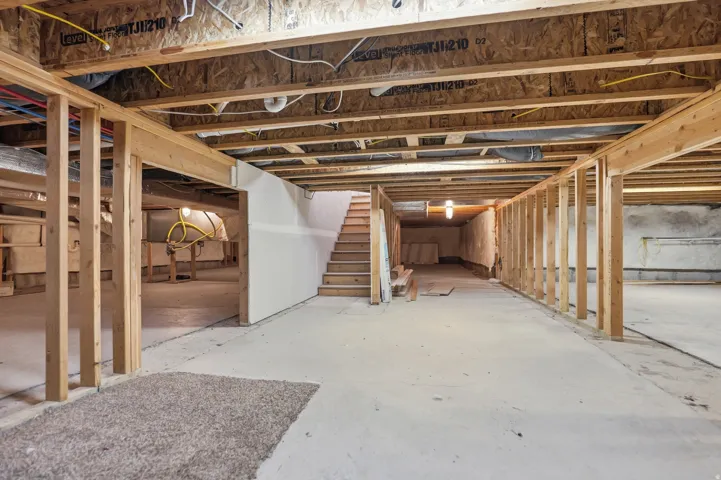 Unfinished basement with concrete flooring, wood framing, exposed ceiling joists, and a visible staircase