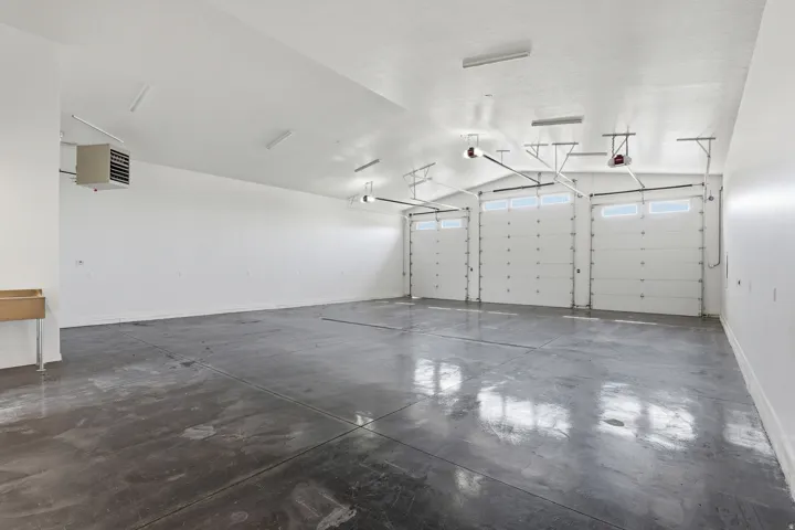 Spacious garage featuring three overhead doors with window panels, polished concrete flooring, overhead fluorescent lighting, and a wall-mounted utility sink