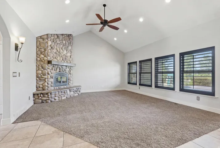 Spacious interior featuring a stone fireplace with hearth, vaulted ceilings, recessed lighting, and a ceiling fan
