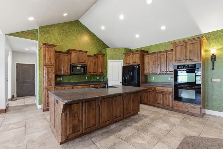 Kitchen featuring wood cabinetry, a central island with integrated sink, black appliances including a double oven and microwave, and recessed lighting