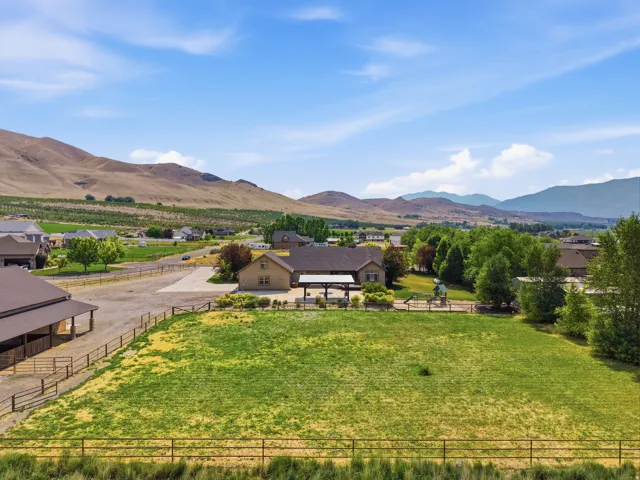 Expansive property featuring a large green space, a tan-sided residence with a covered patio, and a separate barn structure