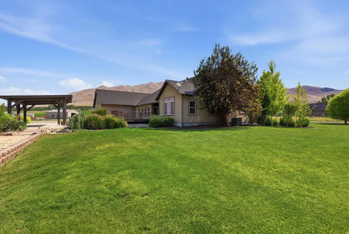 Expansive green lawn surrounds a single-story residence with light-colored siding and a dark shingle roof