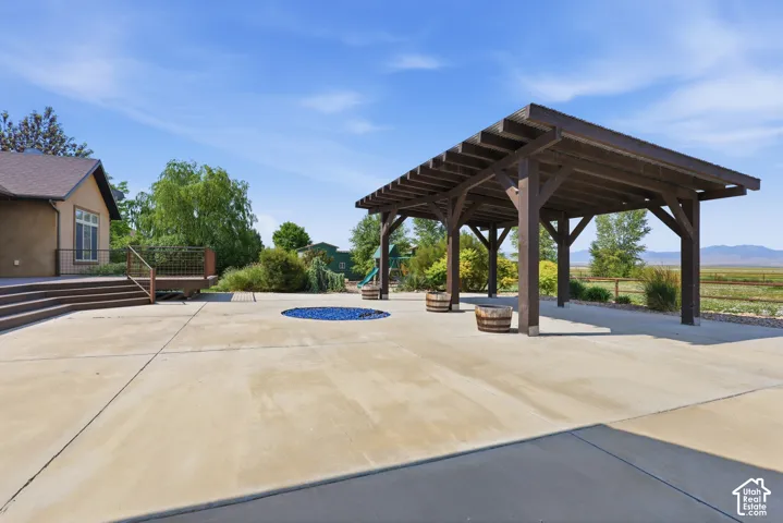 Spacious concrete patio featuring a wood pergola and an integrated circular fire pit with blue glass rocks