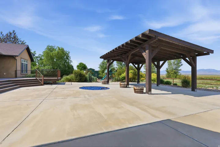 Spacious concrete patio featuring a wood pergola and an integrated circular fire pit with blue glass rocks