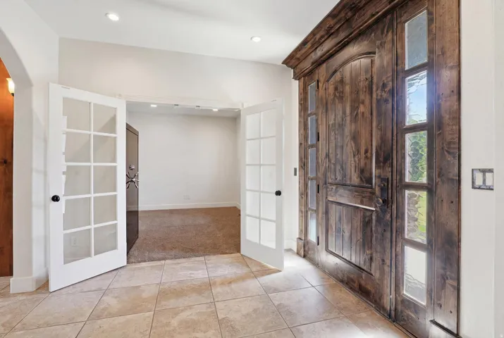 Foyer featuring a grand wood-finish entry door with multiple glass sidelights, light-toned tile flooring, recessed lighting, and a double French door entry to a carpeted room