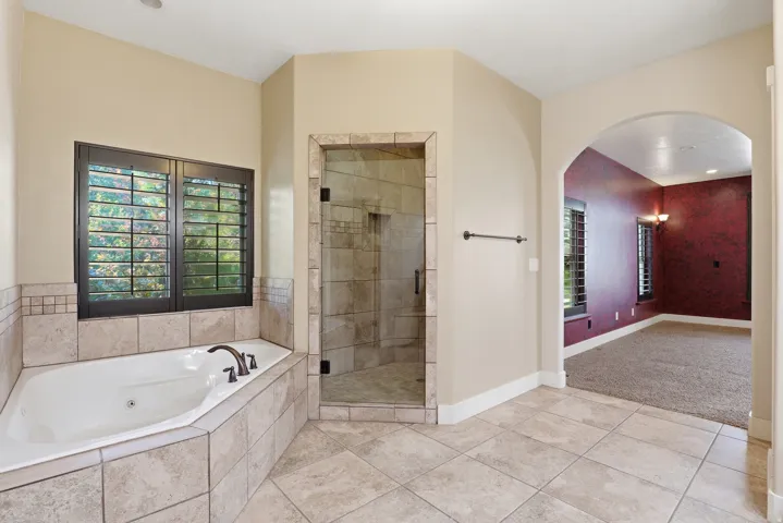 Spacious bathroom featuring a built-in jetted tub with tile surround, a glass-enclosed shower with tile, and large format tile flooring