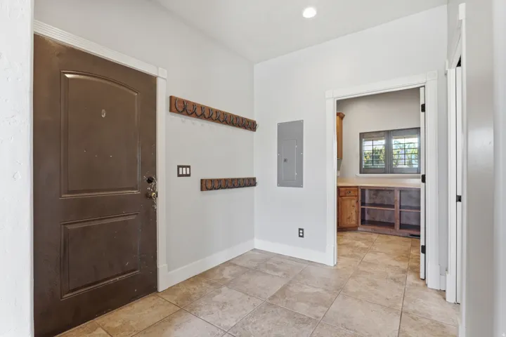 Entryway featuring natural tile flooring, a solid panel door with arched detailing, and two wall-mounted coat racks