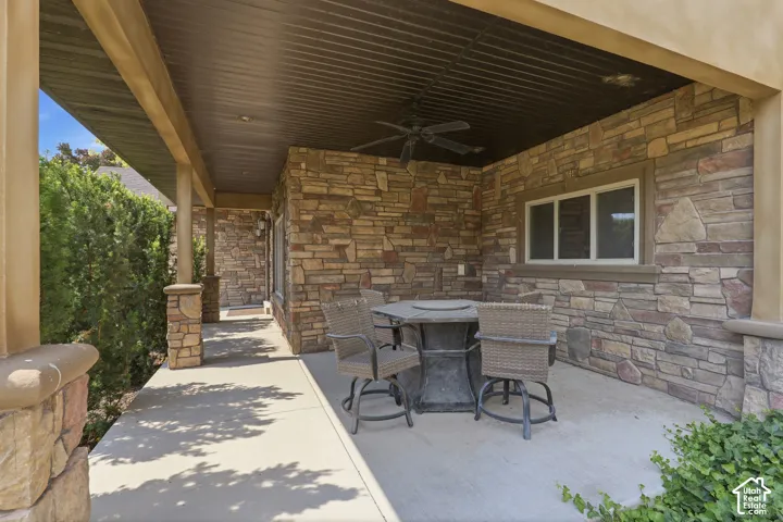 Covered patio featuring stone veneer walls, a corrugated metal ceiling, and a ceiling fan