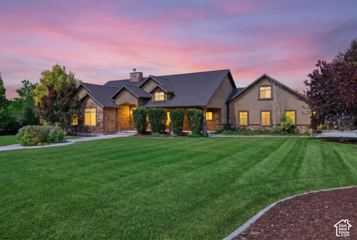 Stucco and stone facade home featuring a dark shingle roof, a prominent chimney, and multiple gables