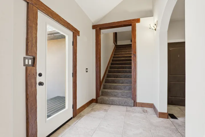 Foyer featuring tile flooring, a glass-paneled entry door with dark hardware, rough-hewn wood trim, and a carpeted staircase with wood risers