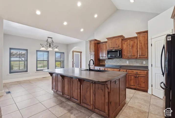 Kitchen featuring a large island with integrated sink, wood cabinetry, tile flooring, and a vaulted ceiling