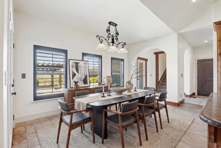 Dining area featuring a dark-finish chandelier, multiple windows with plantation shutters, arched doorways, and tile flooring