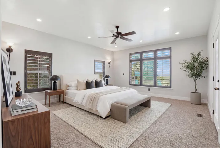 Spacious bedroom featuring plush carpeting, a ceiling fan, recessed lighting, and multiple windows with plantation shutters