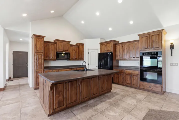 Kitchen featuring a central island with an integrated sink, extensive wood cabinetry, built-in double ovens, and tile flooring