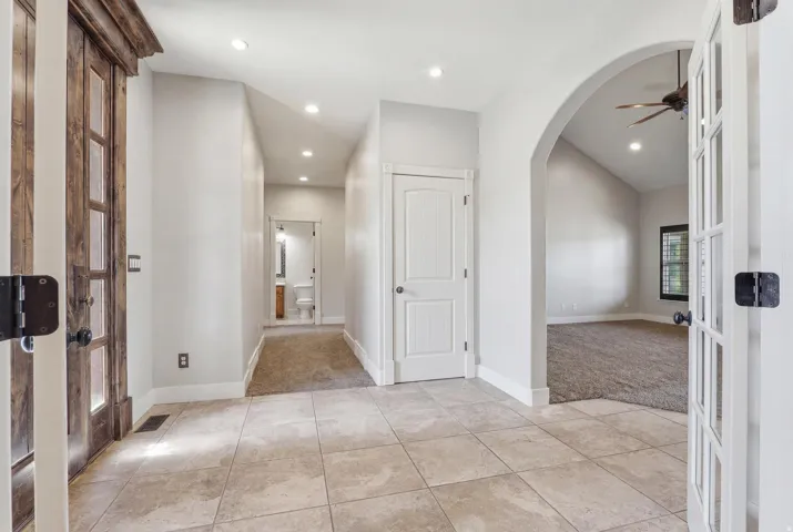 Entryway featuring large format tile flooring, a vaulted ceiling, recessed lighting, and an arched doorway leading to a carpeted room