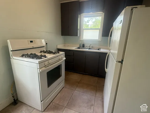 Kitchen featuring a white gas range, a white refrigerator, brown cabinetry, and a white sink with a window overhead