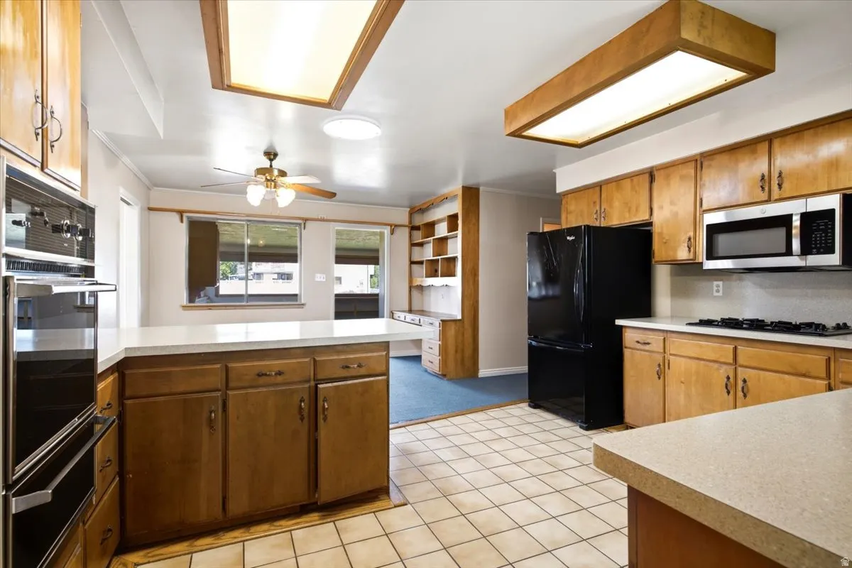 Kitchen featuring wood cabinetry, light-toned countertops, tile flooring, and stainless steel appliances