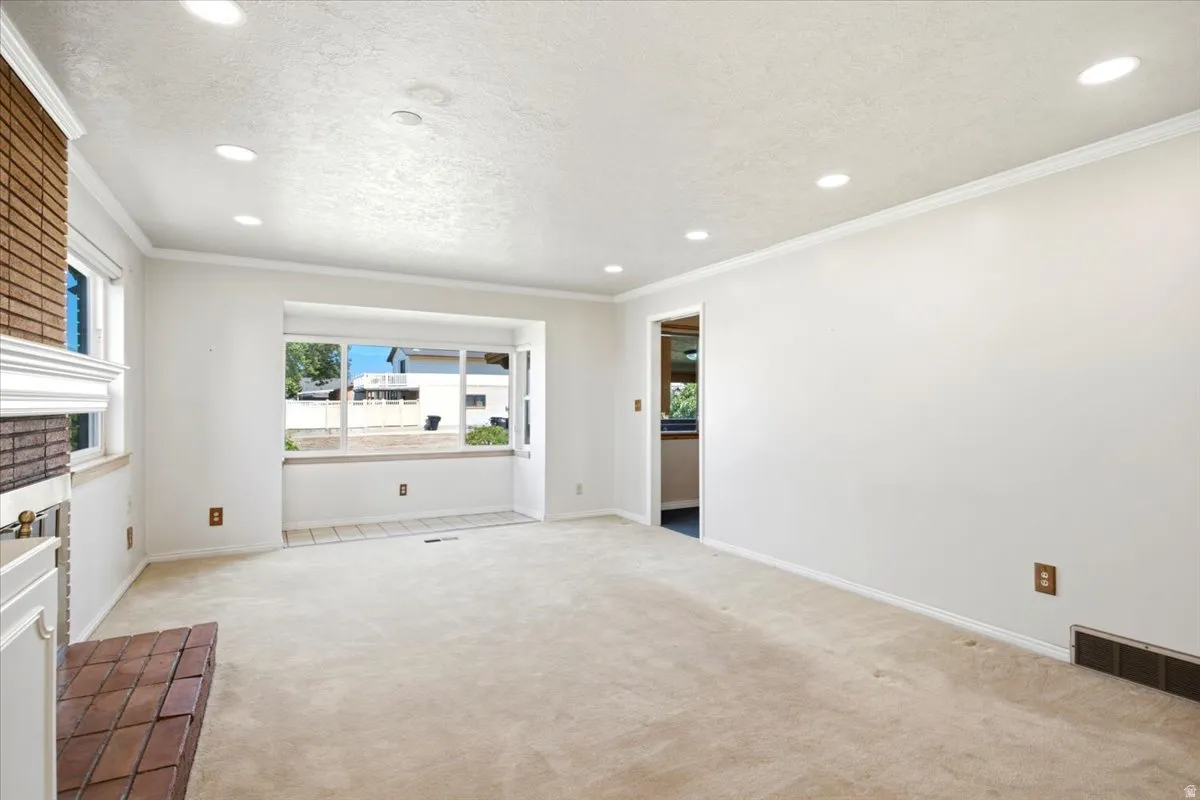 Spacious living area featuring a bay window with tiled flooring, neutral-toned carpet, recessed lighting, and a brick fireplace