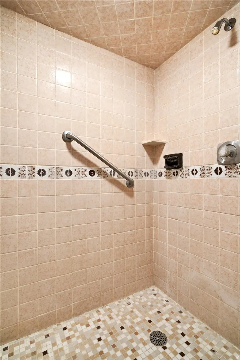 Tiled shower with a decorative mosaic accent band, integrated corner shelf, and a grab bar