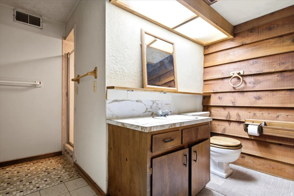 Bathroom featuring a wood-finish vanity with a marbled countertop, an integrated sink, a large mirror, and wood-paneled walls