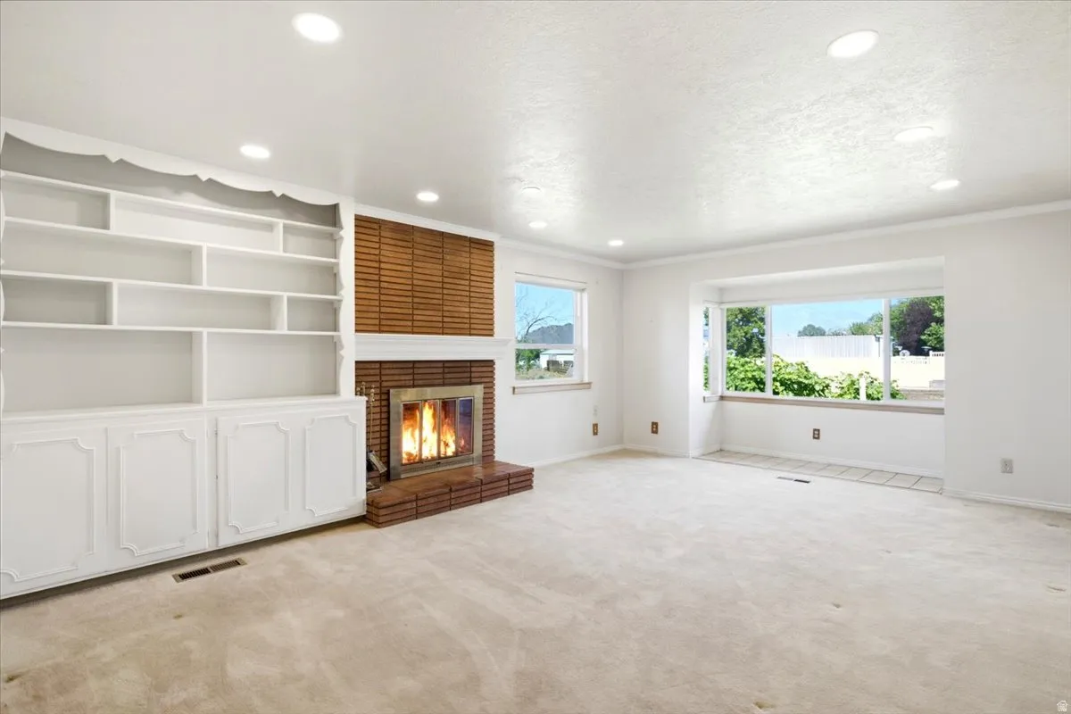 Living area featuring a brick fireplace with a wood mantle, built-in shelving and cabinetry, recessed ceiling lighting, and a bay window