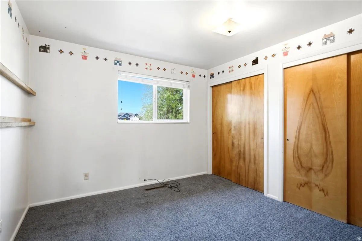 Carpeted room featuring a double window, two wooden sliding closet doors, and built-in wall shelving