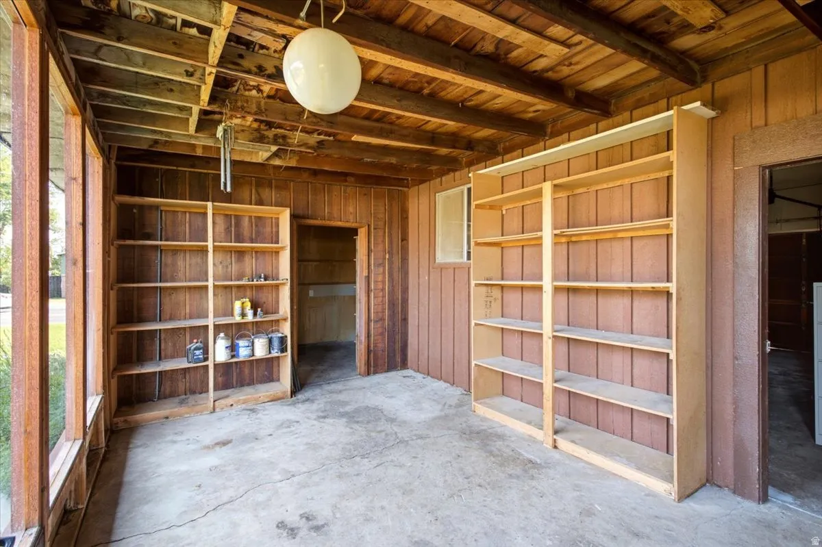 Enclosed porch featuring wood-panel walls, exposed wood beam ceiling, concrete flooring, and built-in shelving