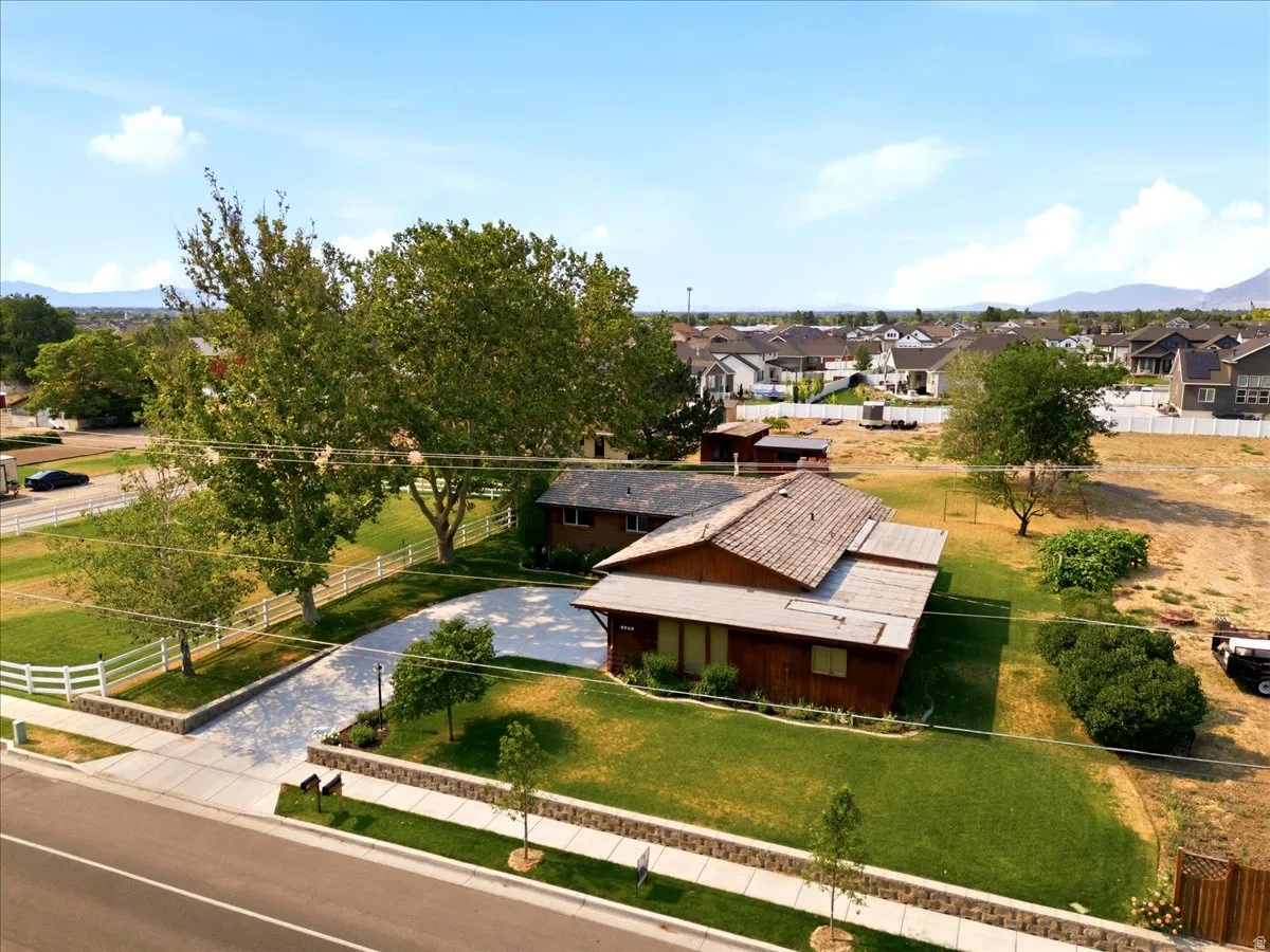 Expansive property featuring a residence with a shingle roof, a large paved driveway, white picket fencing, and mature trees