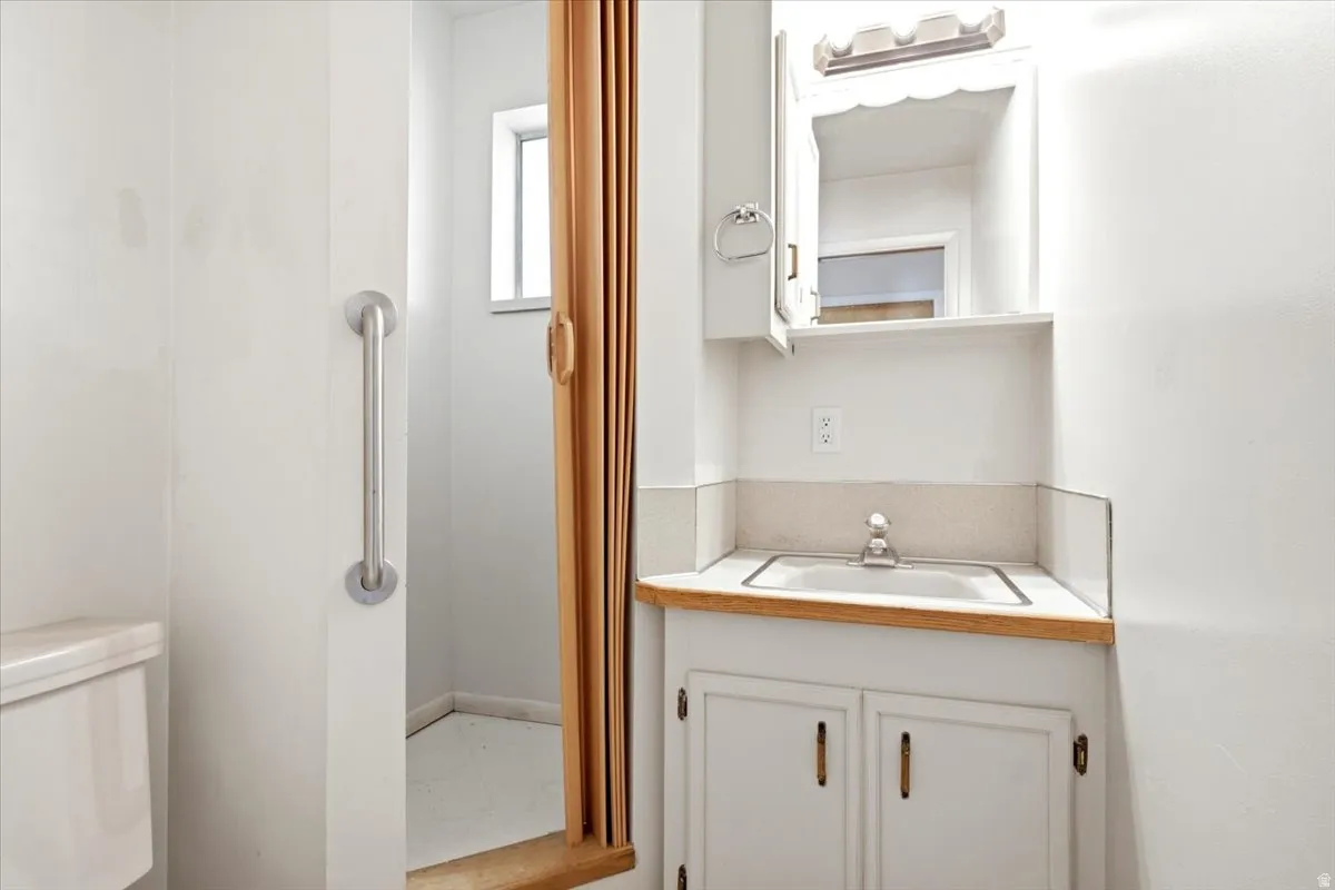 Bathroom vanity featuring a built-in sink, light wood-finish countertop, white cabinetry with brass hardware, and a medicine cabinet with integrated lighting