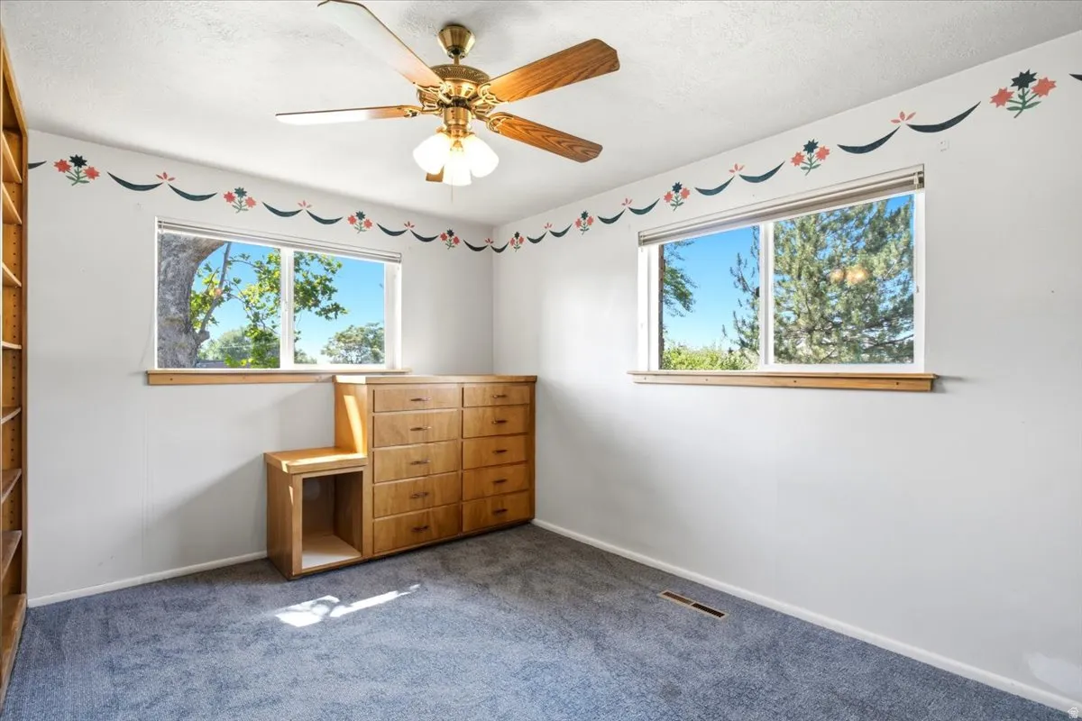 Light-filled room featuring two windows, blue carpeting, and a ceiling fan with integrated lighting