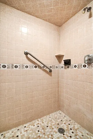 Tiled shower with a decorative mosaic accent band, integrated corner shelf, and a grab bar