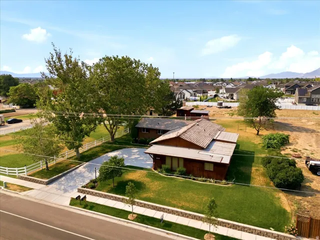Expansive property featuring a residence with a shingle roof, a large paved driveway, white picket fencing, and mature trees