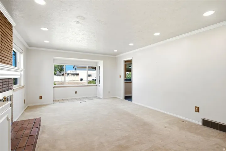 Spacious living area featuring a bay window with tiled flooring, neutral-toned carpet, recessed lighting, and a brick fireplace