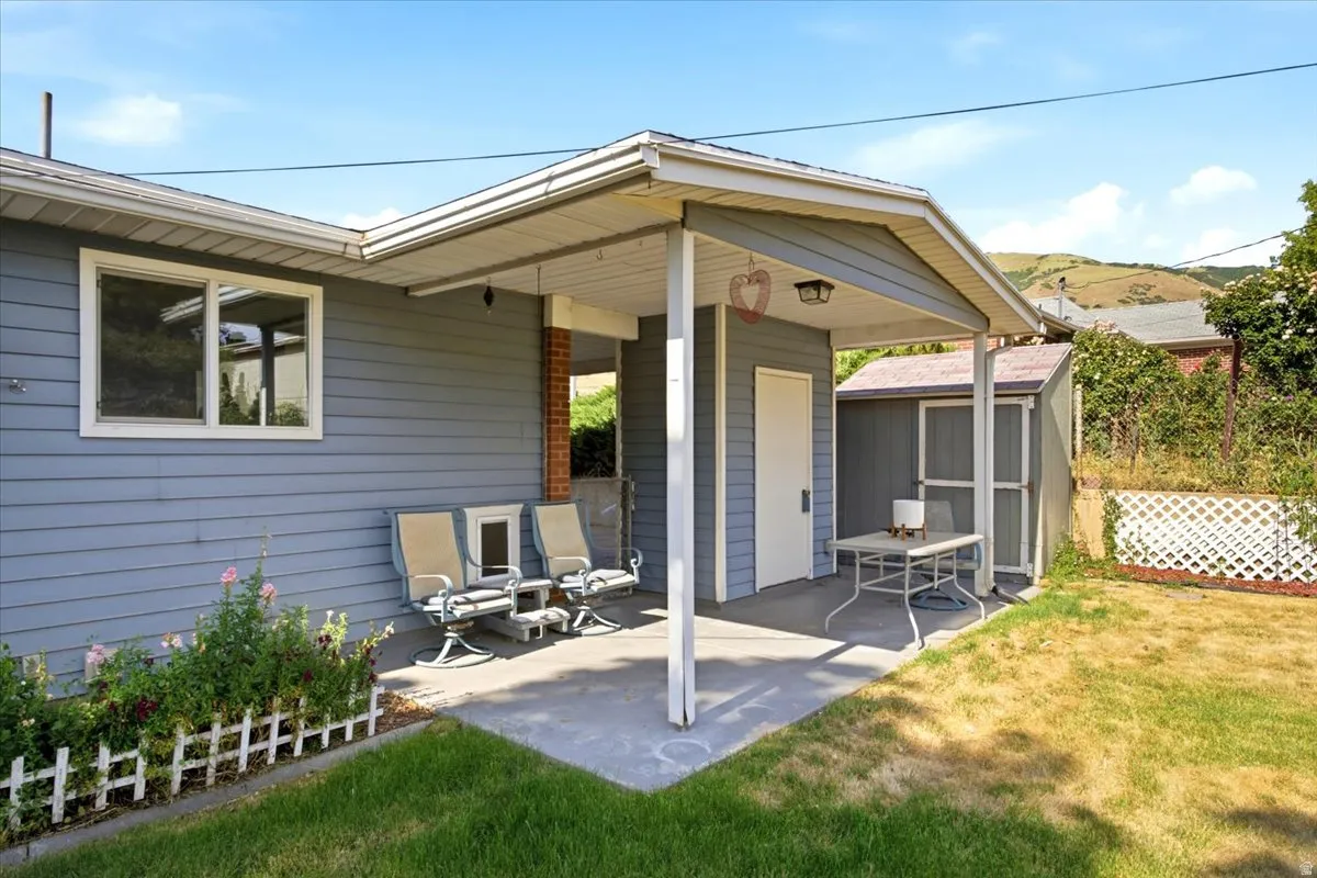 Covered patio with shed overlooking a nice backyard of flowers, grapes, and gardening spaces.