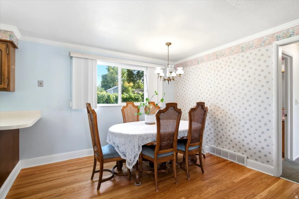 Dining area with wood-finish flooring, a brass chandelier, and vintage wallpaper with a floral border