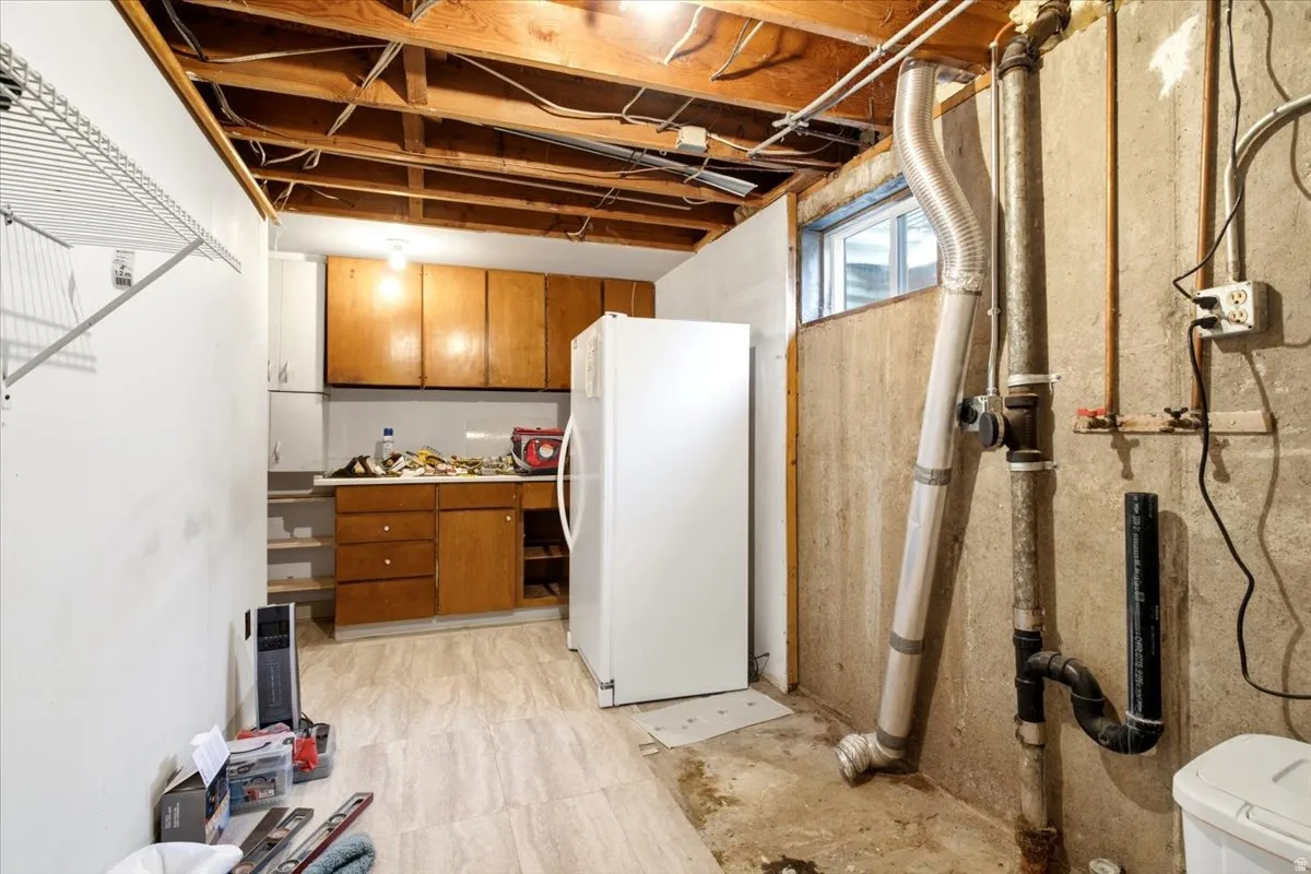 Unfinished basement space for laundry and storage with a small window and a white freezer
