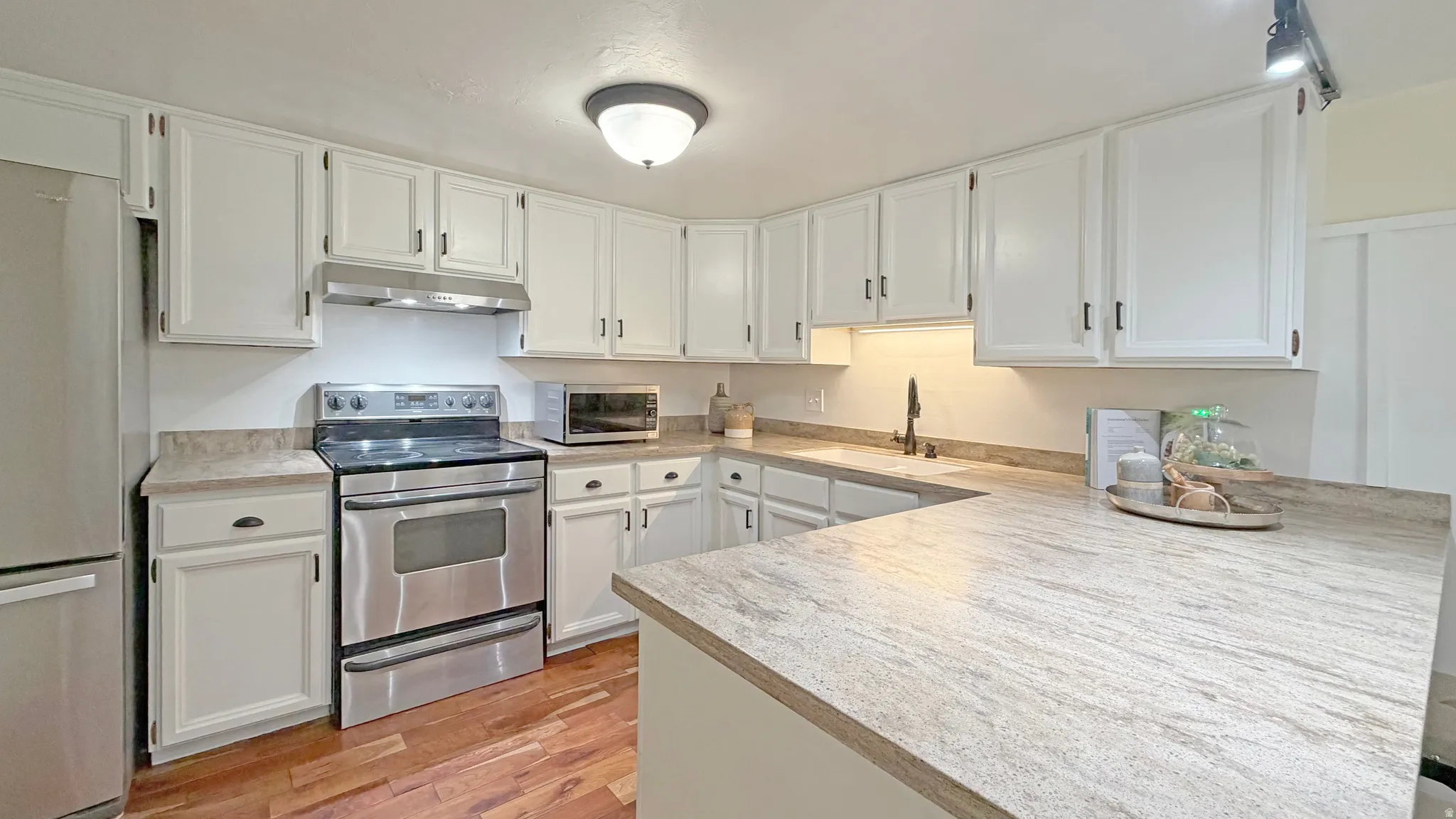 Kitchen featuring wood-finish flooring, white cabinetry with dark hardware, stainless steel appliances, granite countertops with a matching backsplash