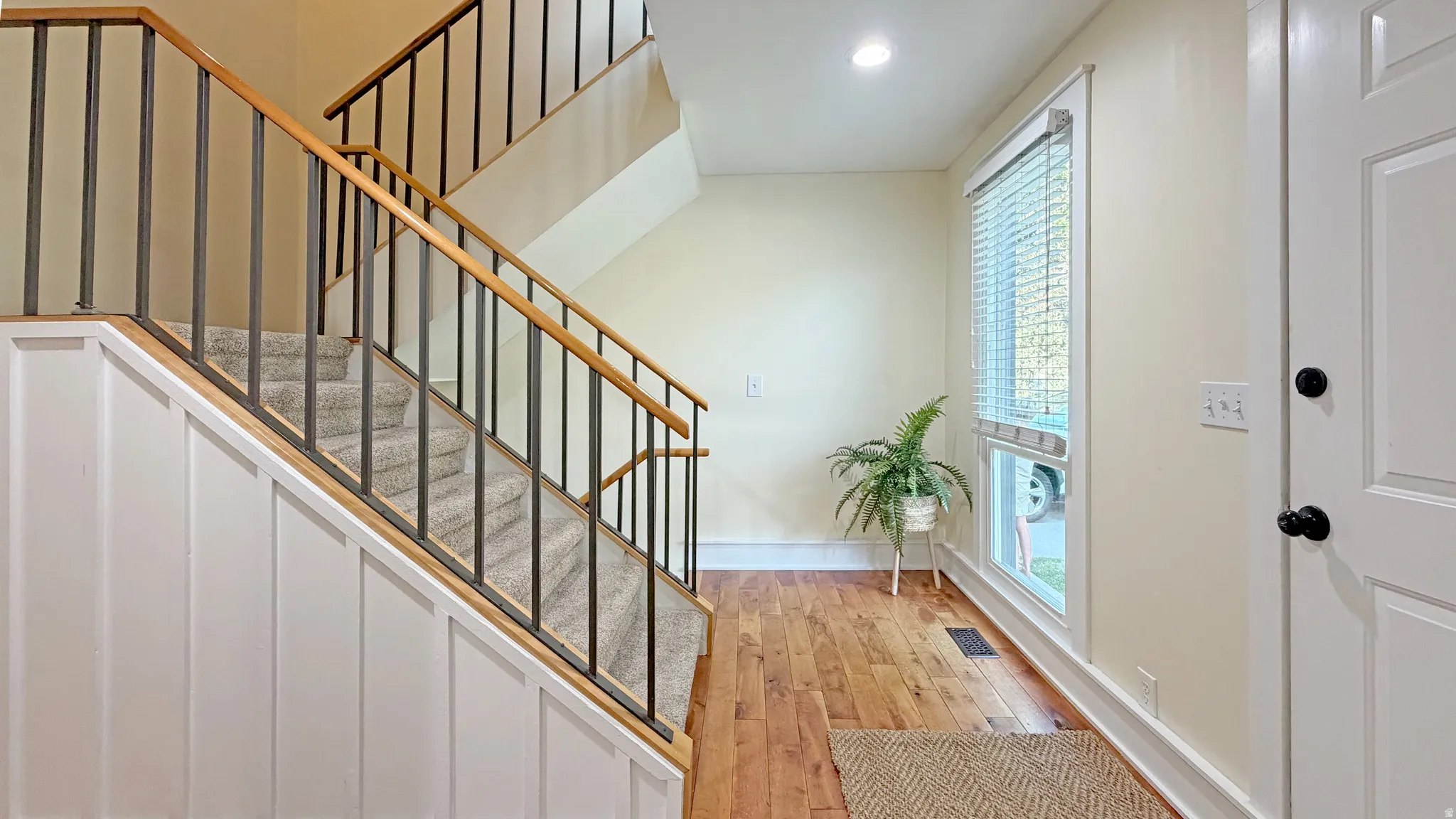Foyer featuring wood-finish flooring, a contemporary staircase with metal balusters and wood handrails, carpeted treads, and a white paneled wall