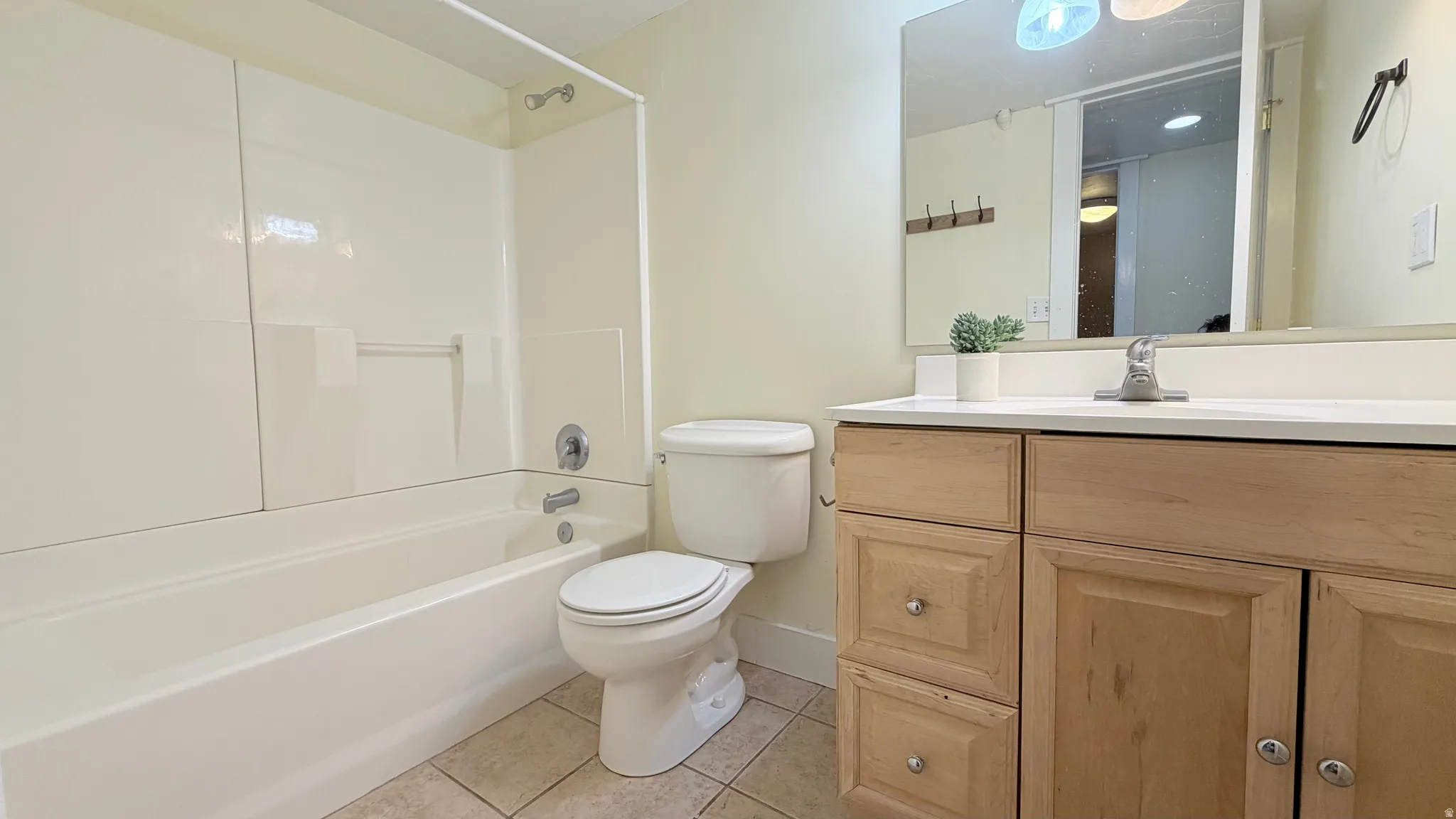 Bathroom featuring a white bathtub with a wall-mounted shower, and a light wood-finish vanity with a white countertop