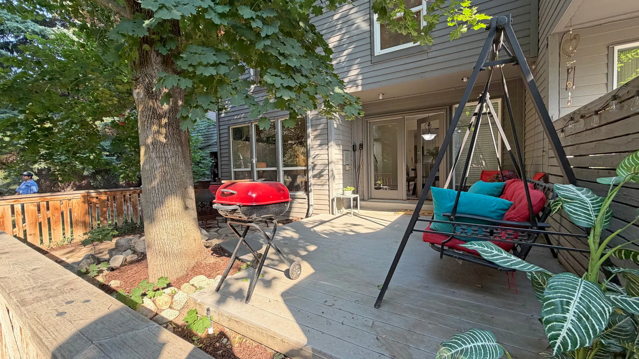 Expansive wood-finish deck with mature tree, built-in planter, and sliding glass door access to the interior
