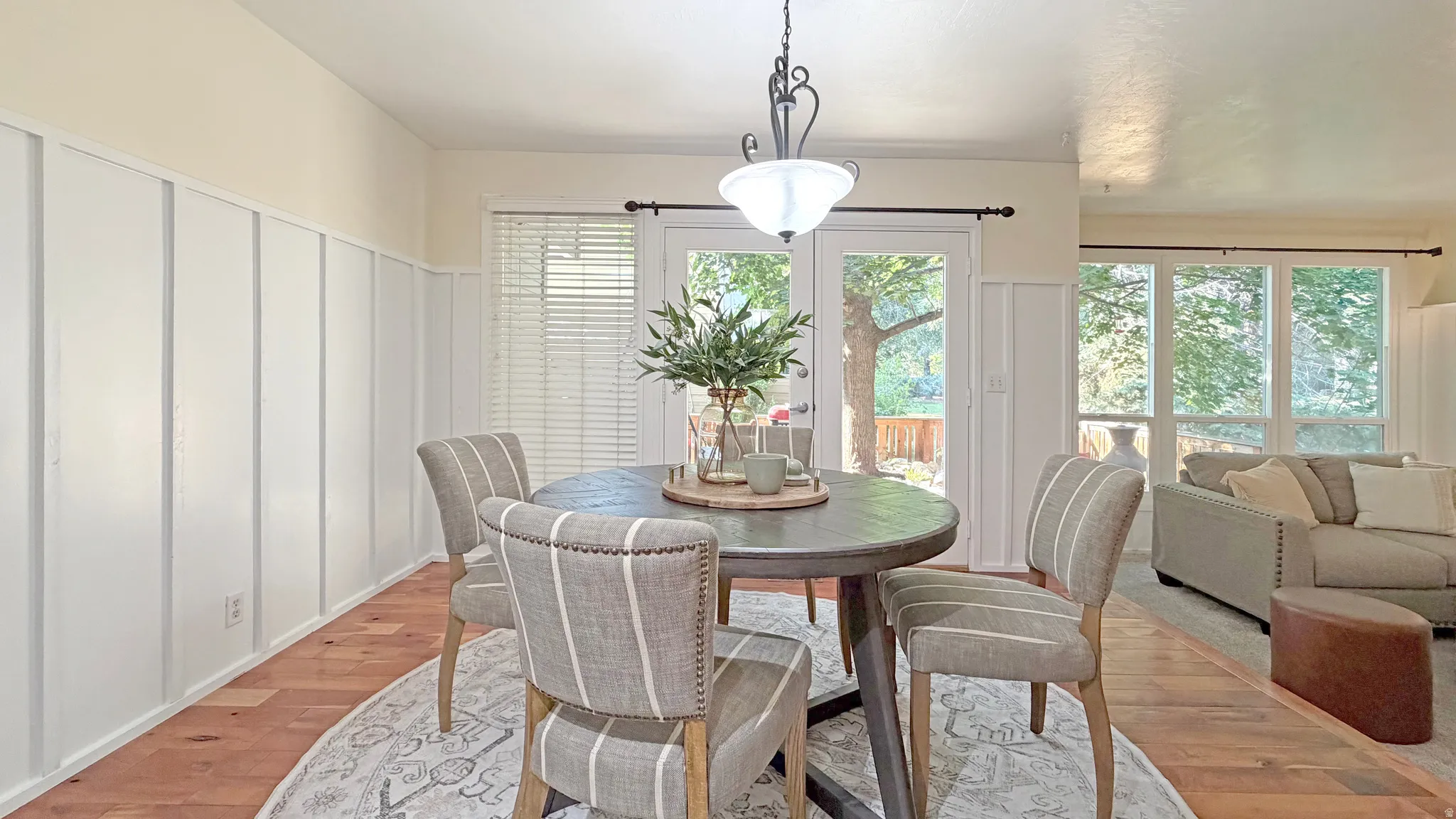 Dining area featuring wood-finish flooring, white board and batten wall paneling, and a contemporary chandelier