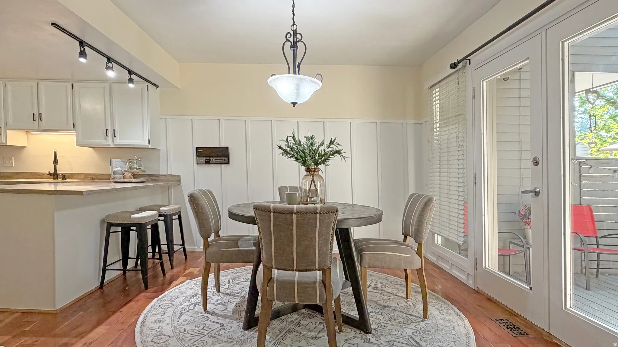 Dining area featuring hardwood flooring, a decorative ceiling light fixture, and white board and batten wall paneling