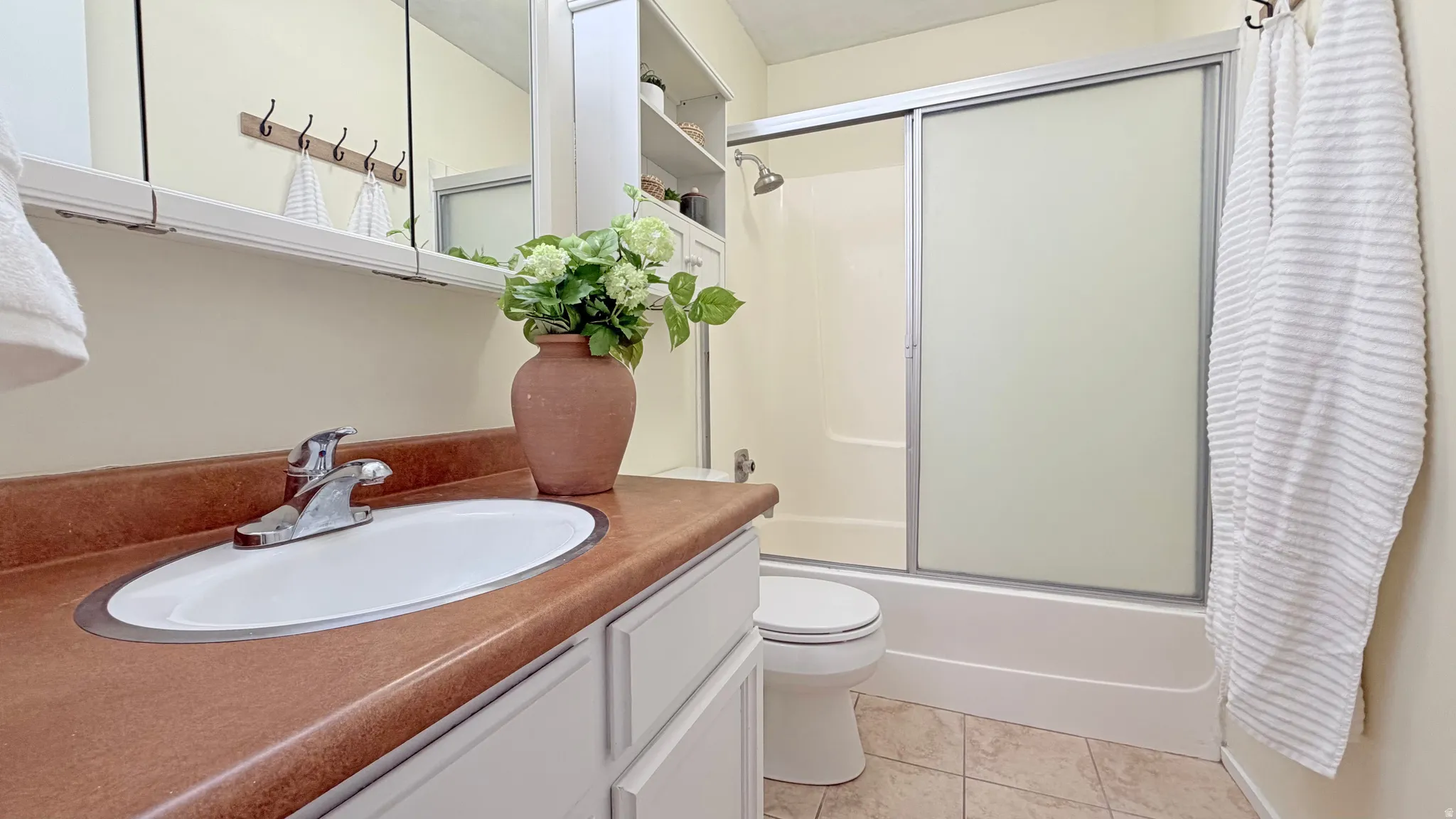 Bathroom featuring a light-toned vanity with an oval sink and chrome faucet, a medicine cabinet with mirrored doors, a shower-tub combination with sliding frosted glass doors, and light-toned floor tiling